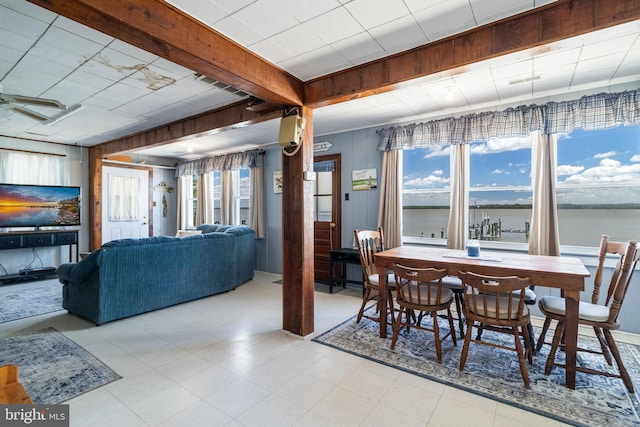 dining space with a wealth of natural light, beamed ceiling, a water view, and light tile floors