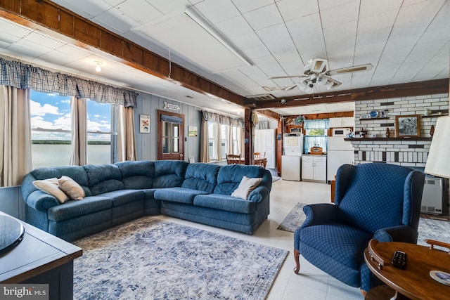 tiled living room featuring ceiling fan, a water view, and brick wall