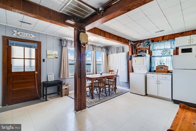 kitchen with light tile flooring, white cabinets, white appliances, and stacked washer and clothes dryer