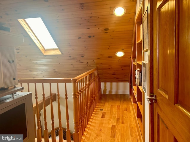 corridor with wood walls, wooden ceiling, vaulted ceiling with skylight, and light wood-type flooring