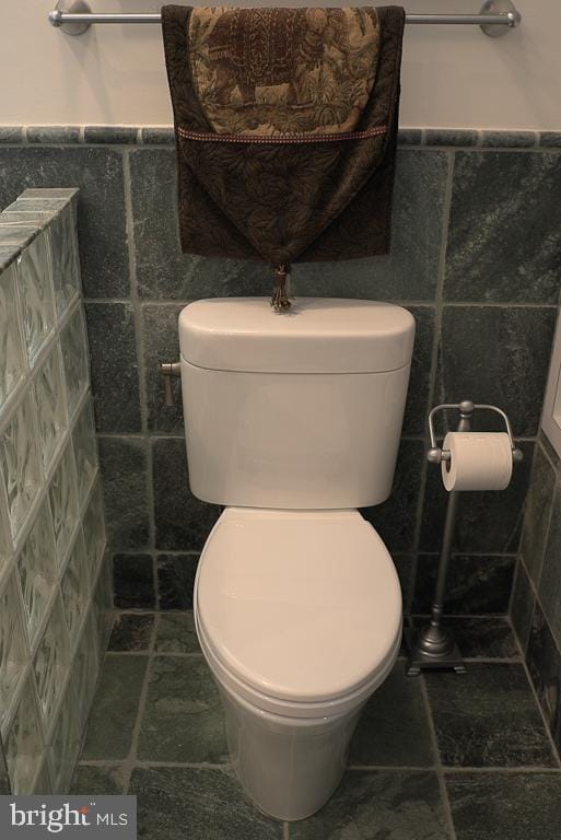 bathroom with tile flooring, toilet, and tile walls