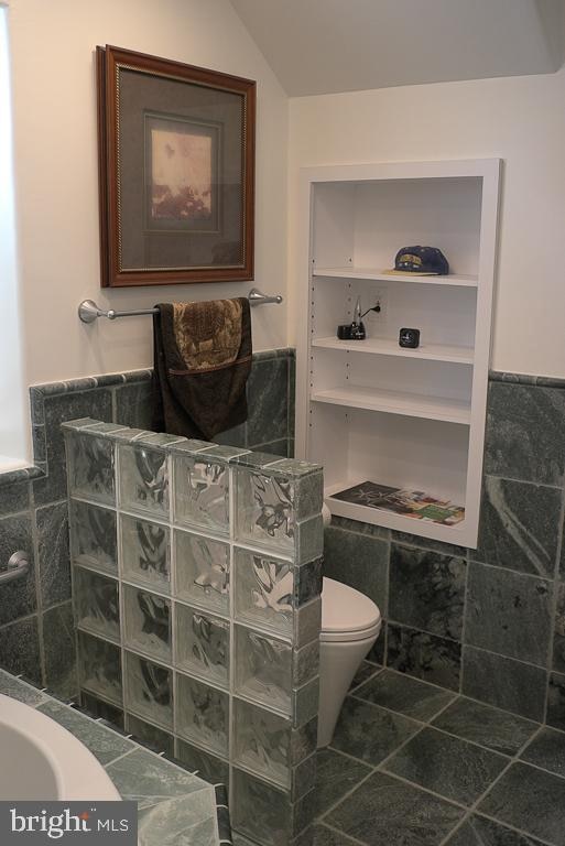 bathroom with tile flooring, tile walls, toilet, and a shower