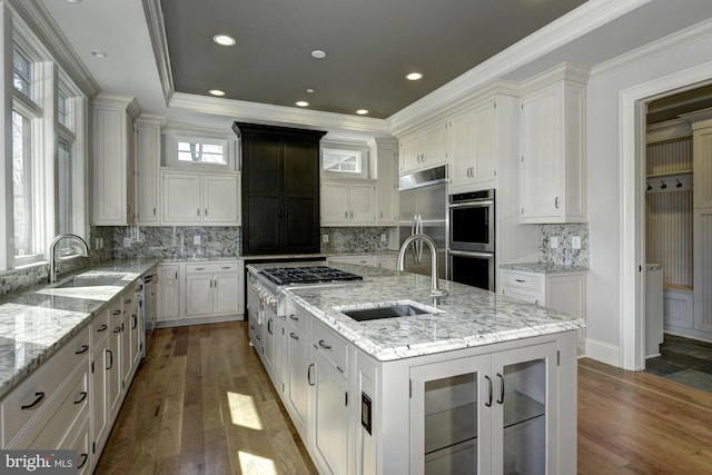 kitchen with appliances with stainless steel finishes, a center island with sink, decorative backsplash, and hardwood / wood-style floors