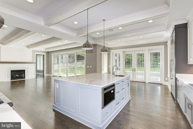 kitchen with french doors, hanging light fixtures, light stone countertops, a kitchen island with sink, and white cabinets