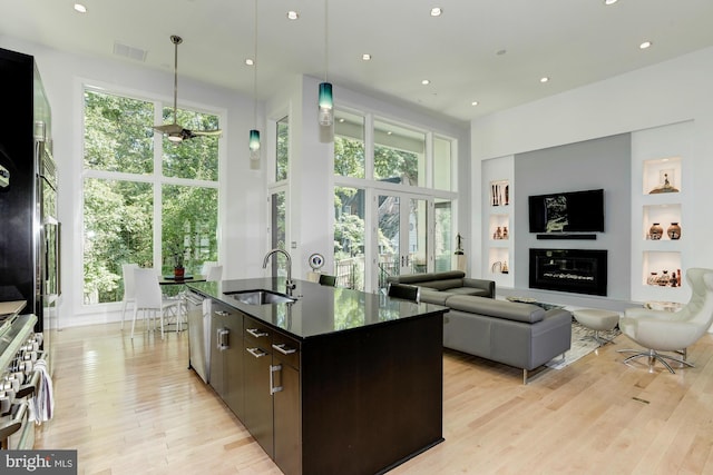 kitchen with light hardwood / wood-style flooring, dark brown cabinets, appliances with stainless steel finishes, a kitchen island with sink, and sink