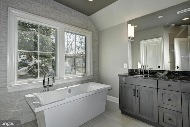 bathroom featuring a bathtub, tile patterned floors, vanity, and vaulted ceiling