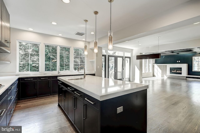 kitchen featuring french doors, sink, decorative light fixtures, light hardwood / wood-style flooring, and a kitchen island with sink