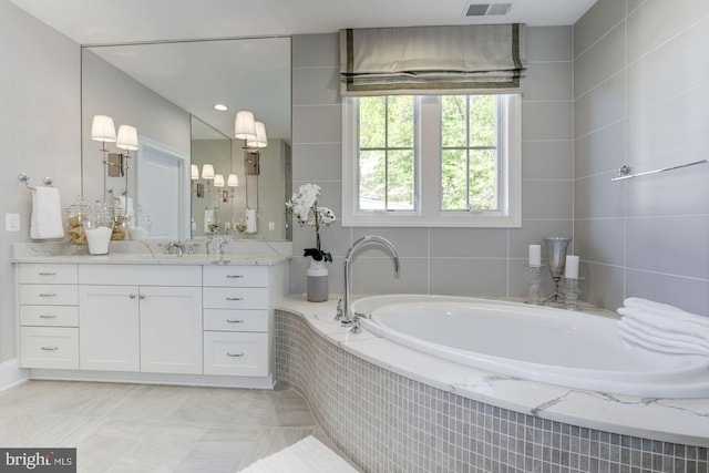 bathroom with tile walls, tiled bath, vanity, and tile patterned flooring