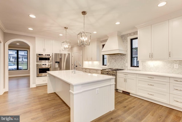 kitchen featuring high quality appliances, premium range hood, a kitchen island with sink, and white cabinetry