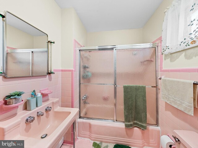 bathroom featuring combined bath / shower with glass door and tile walls