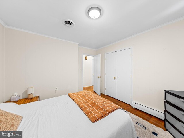 bedroom with crown molding, a closet, wood-type flooring, and a baseboard heating unit