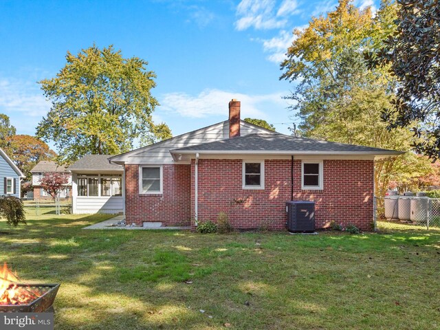 rear view of property with a lawn, a sunroom, and central AC unit