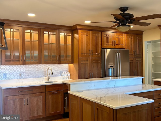 kitchen with backsplash, sink, ceiling fan, stainless steel fridge, and light stone counters