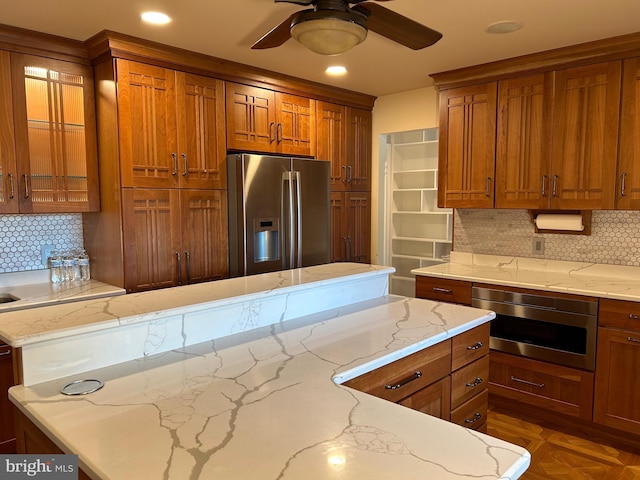 kitchen with decorative backsplash, ceiling fan, light stone countertops, and stainless steel appliances