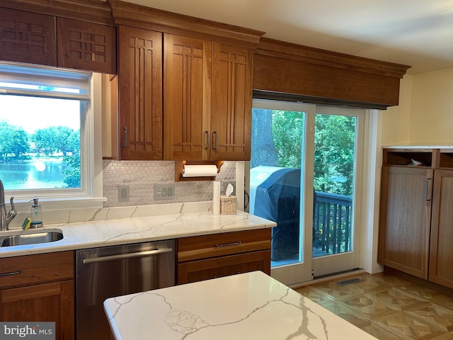 kitchen featuring stainless steel dishwasher, a healthy amount of sunlight, and light stone counters