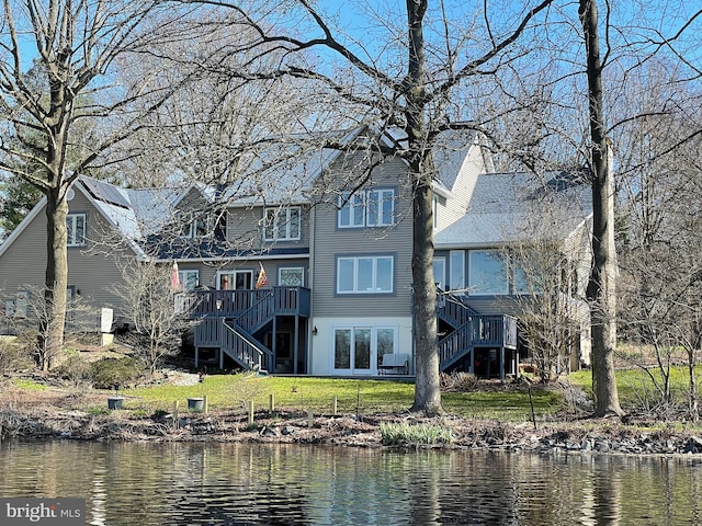 rear view of house with a deck with water view and a lawn