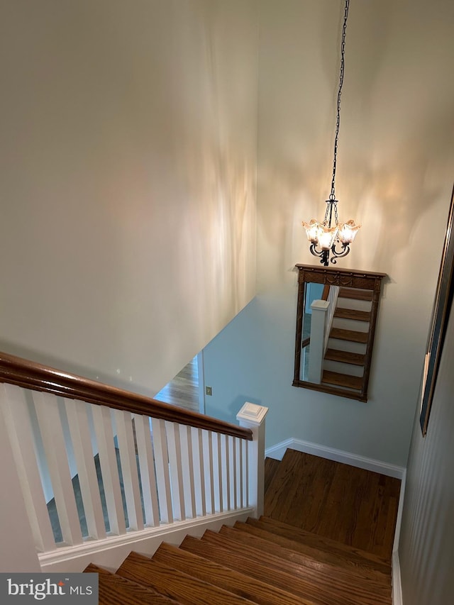 stairway with hardwood / wood-style floors and a notable chandelier