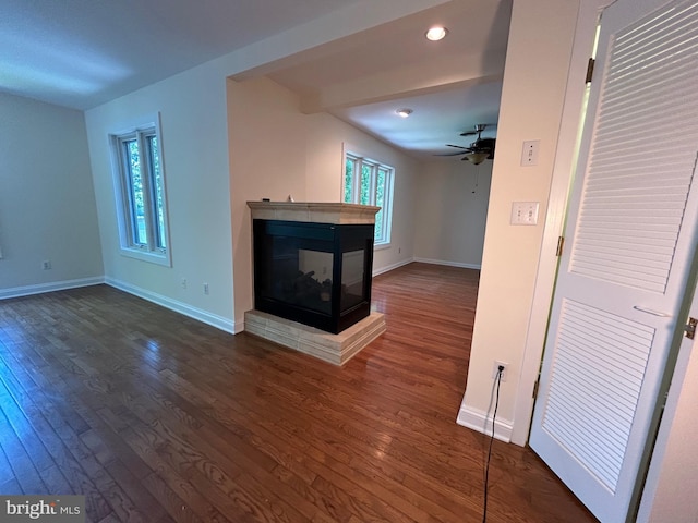 unfurnished living room featuring a multi sided fireplace, ceiling fan, and dark wood-type flooring