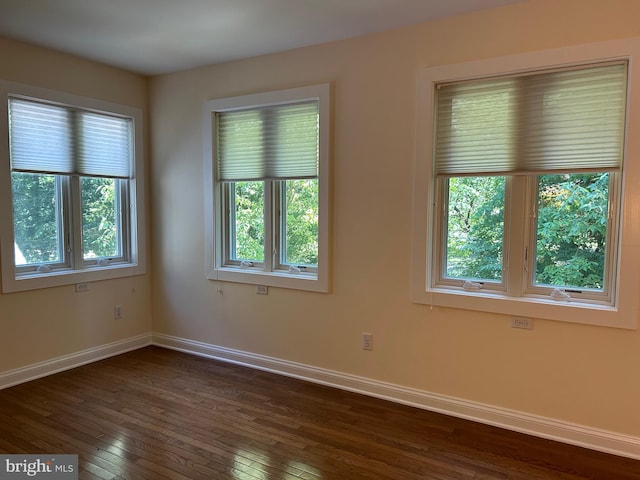 empty room with a wealth of natural light and dark hardwood / wood-style floors