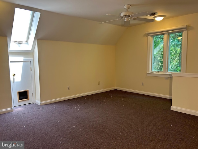 additional living space with dark carpet, ceiling fan, and vaulted ceiling with skylight