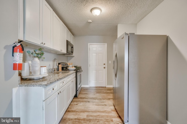 kitchen with light wood-type flooring, white cabinetry, sink, and appliances with stainless steel finishes