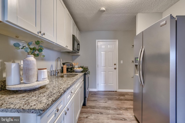 kitchen with appliances with stainless steel finishes, light wood-type flooring, white cabinetry, and sink