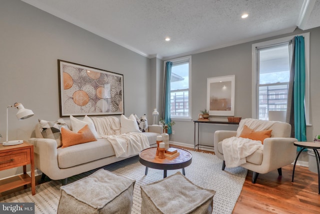 living room with plenty of natural light, light wood-type flooring, a textured ceiling, and ornamental molding