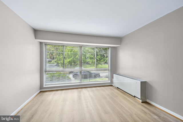 unfurnished room featuring plenty of natural light, radiator heating unit, and light wood-type flooring