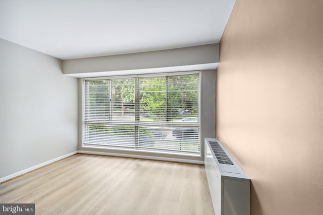 unfurnished room with light hardwood / wood-style floors, radiator heating unit, and plenty of natural light