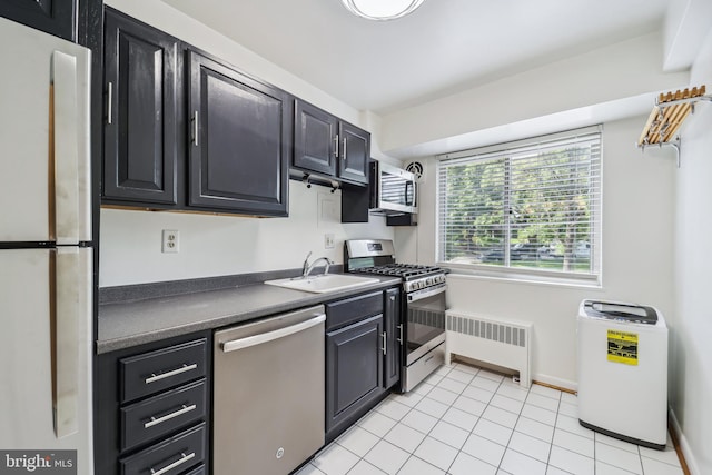 kitchen with appliances with stainless steel finishes, radiator heating unit, light tile patterned floors, and sink