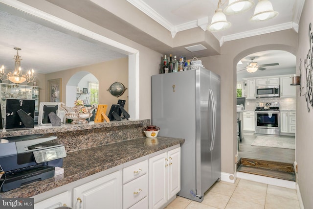 kitchen featuring dark stone counters, ceiling fan with notable chandelier, stainless steel appliances, decorative light fixtures, and white cabinets