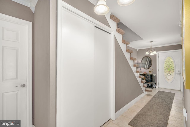 foyer entrance featuring light tile patterned flooring, crown molding, and an inviting chandelier