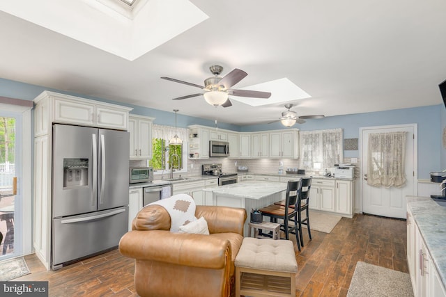 kitchen with dark wood-type flooring, hanging light fixtures, a skylight, appliances with stainless steel finishes, and a kitchen island