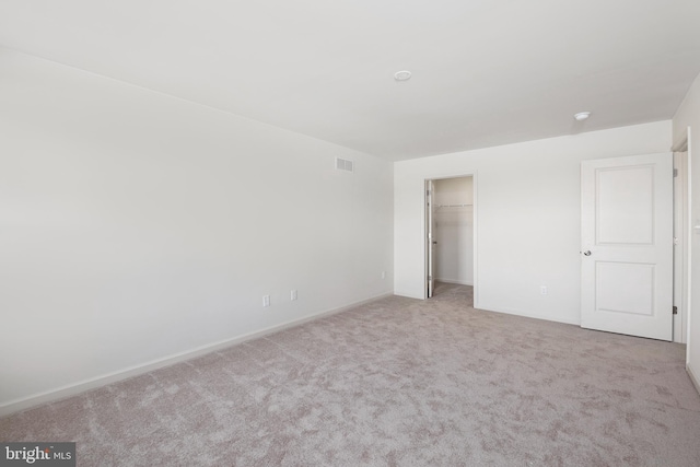 unfurnished bedroom with light colored carpet, a walk in closet, and a closet