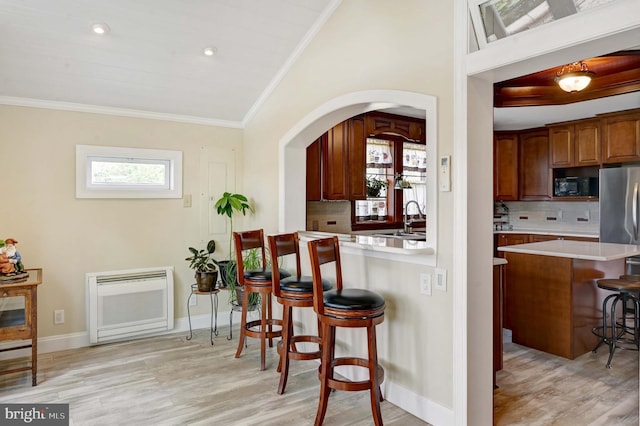 kitchen featuring crown molding, a kitchen breakfast bar, tasteful backsplash, and light wood-type flooring