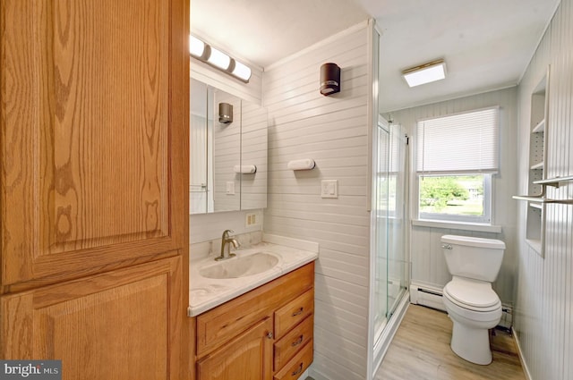 bathroom featuring a baseboard radiator, vanity with extensive cabinet space, toilet, a shower with shower door, and wood-type flooring