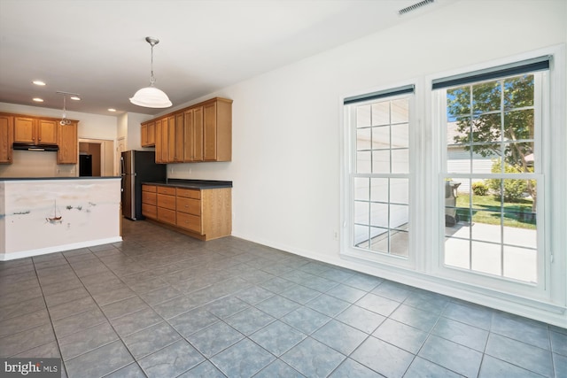 kitchen featuring stainless steel refrigerator, hanging light fixtures, and dark tile patterned flooring