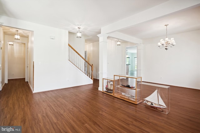 unfurnished living room featuring a notable chandelier, dark hardwood / wood-style flooring, and ornate columns