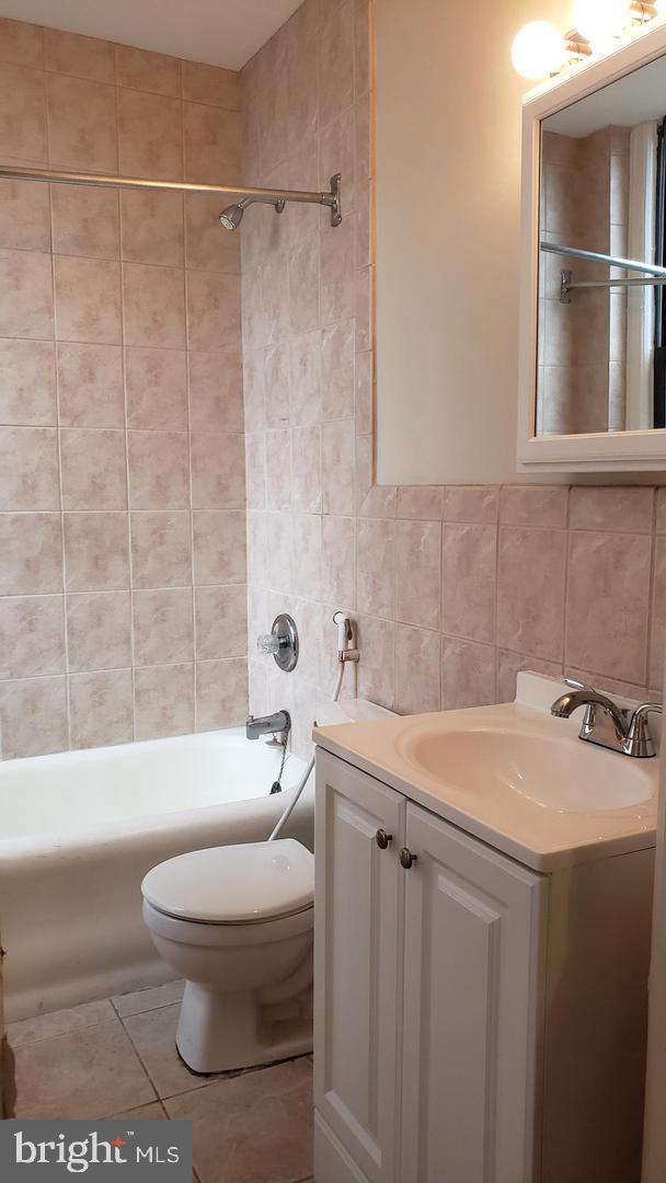 full bathroom with tiled shower / bath combo, tile patterned floors, toilet, vanity, and tile walls