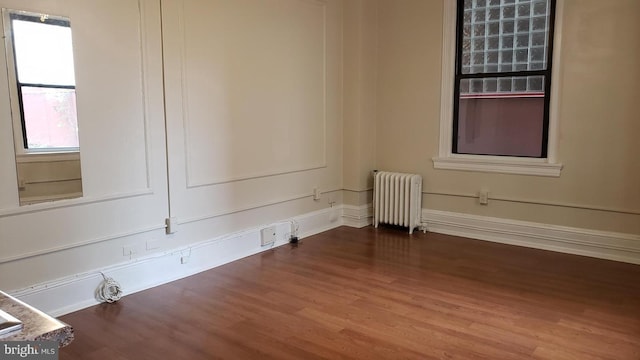 empty room featuring wood-type flooring and radiator heating unit