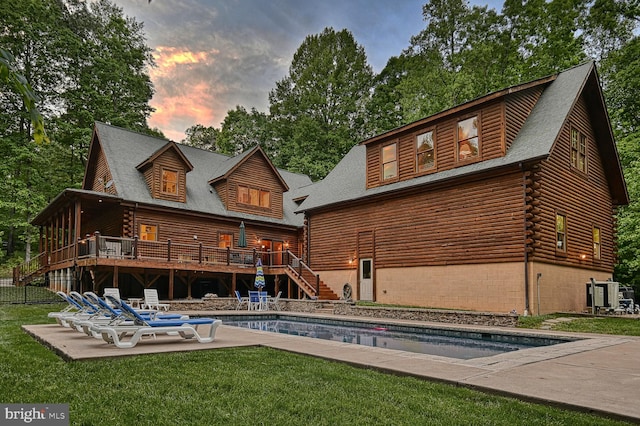 back house at dusk with a swimming pool side deck, a patio, central AC unit, and a lawn