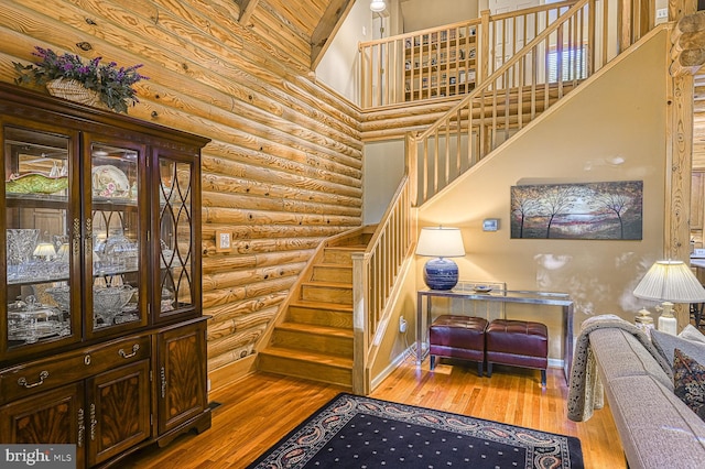 stairway with log walls, high vaulted ceiling, and wood-type flooring