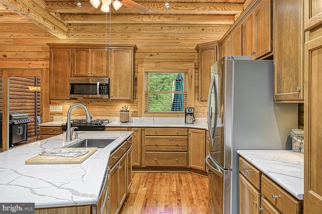 kitchen featuring appliances with stainless steel finishes, light hardwood / wood-style floors, rustic walls, and a kitchen island with sink