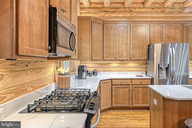 kitchen featuring rustic walls, appliances with stainless steel finishes, and light hardwood / wood-style flooring