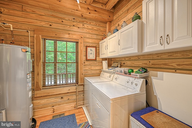 washroom featuring cabinets, electric water heater, washing machine and dryer, rustic walls, and light hardwood / wood-style floors