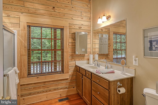 bathroom with vanity, hardwood / wood-style floors, toilet, a shower with shower door, and wood walls