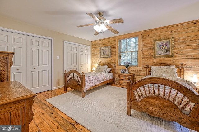 bedroom with ceiling fan, light wood-type flooring, wooden walls, and multiple closets