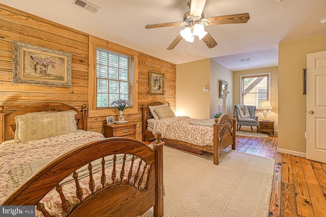 bedroom featuring ceiling fan, wooden walls, and light hardwood / wood-style floors