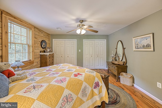 bedroom with wood walls, ceiling fan, two closets, and hardwood / wood-style flooring