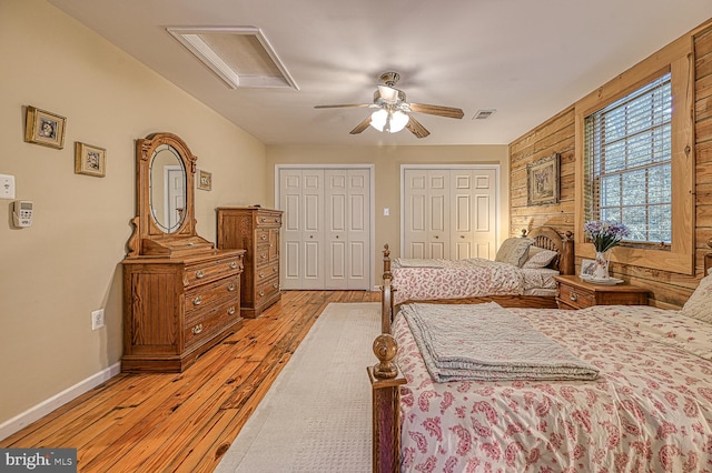 bedroom featuring ceiling fan, wooden walls, light hardwood / wood-style floors, and two closets